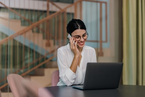 Person smiling at her laptop while on the phone