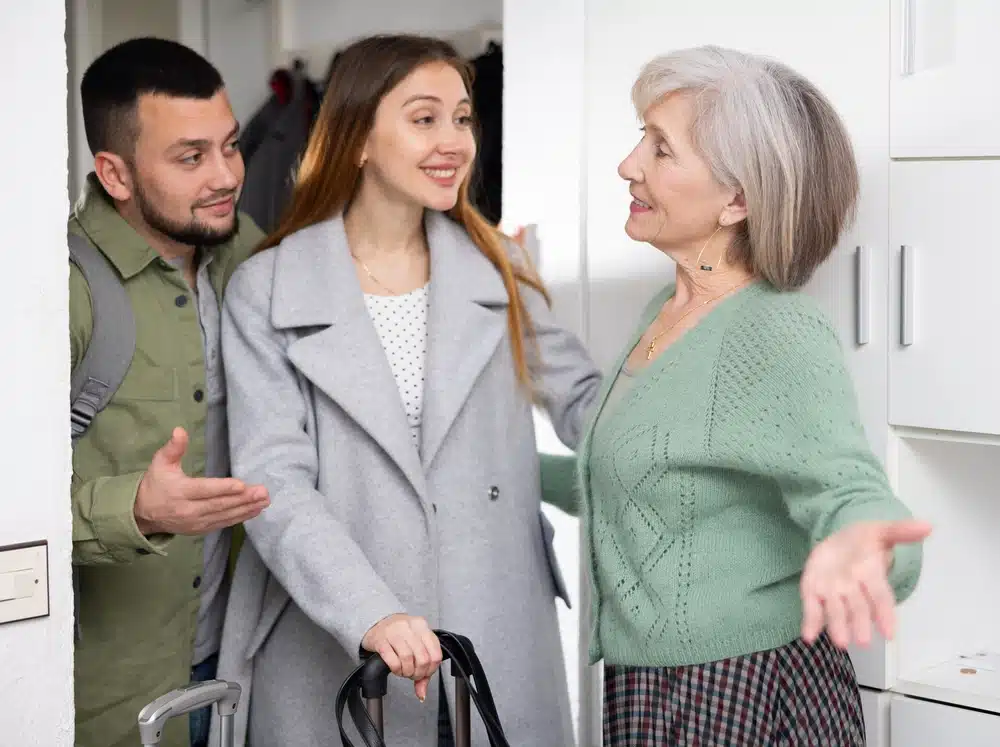 Young couple being greeted by an older woman at a home entrance