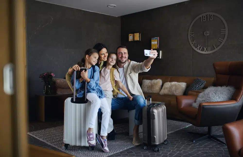 Family Selfie in Hotel Lobby: A family of four taking a selfie in a hotel lobby with their luggage.